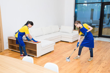 professional cleaning service. Two women in working uniform, in aprons, divide the cleaning of the kitchen of a private house, cottage. Washing floor