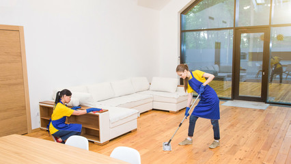 professional cleaning service. Two women in working uniform, in aprons, divide the cleaning of the kitchen of a private house, cottage. Washing floor