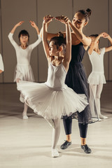 doing practice and training ballet dance with coach teacher woman in tutu skirt, teaching little girl beginner in studio