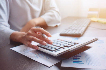 The hand of Asian woman is pressing calculator and prepare information for report to correct. While still holding a silver pen in finger. When calculated completed, can be recorded immediately.