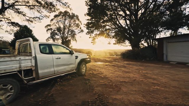 A pick up truck sits idle on a free range farm backlit by a vibrant sunrise. Dolly in