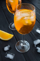 Aperol spritz cocktail in wine glasses on the black wooden background. Location vertical. Closeup.