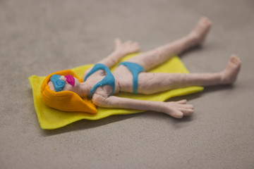 toy blonde from multi-colored dough in a blue bathing suit and glasses sunbathes on a towel on a gray kitchen table close-up 