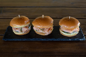 Small burgers with salmon fillet and brie bread on a stone plate