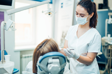 Young female dentist looking for spoiled teeth, patient want to have perfect smile, careful treatment by professional doctor
