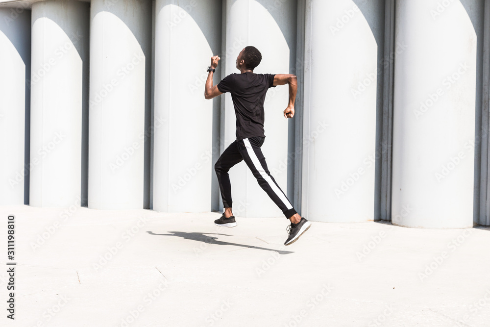 Sticker Athletic young afroamerican man running on the promenade. Black Male runner sprinting outdoors. Healthy lifestyle concept.