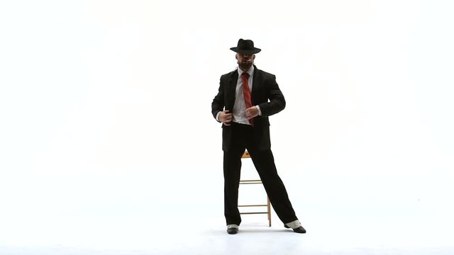 Elegant man in a black hat is dancing an erotic dance. He uses a chair and a cigarette. White background. Close up, slow motion.