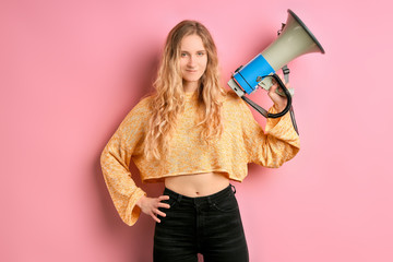 young blond feminist girl using megaphone or loud speaker to promote feminism to society, pink...