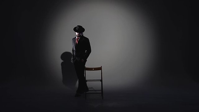 Elegant man in a black hat is dancing an erotic dance. Spotlight on a black background. Close up, slow motion.