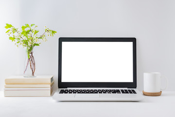 Office workspace with laptop mockup, books, spring flowers in a vase, office supplies on a light background