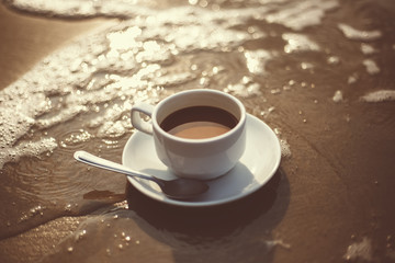 hot cup of coffee on  sand in the beach and sea water flow.