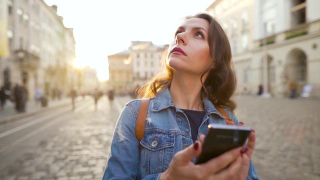 Woman walking down an old street using smartphone and takes photos of sights at sunset. Slow motion