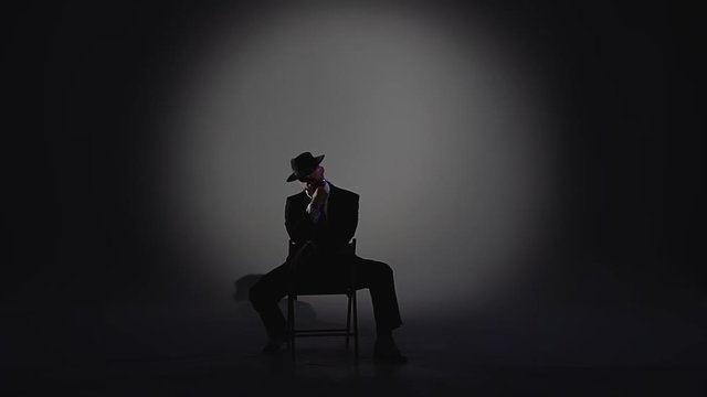 Elegant man in a black hat is dancing an erotic dance. Spotlight on a black background. Close up, slow motion.