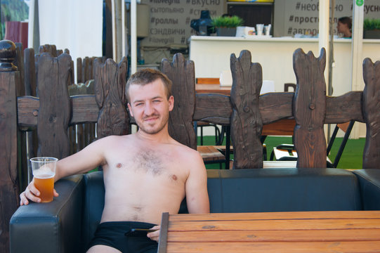 A young man sits in the recreation area in a beach cafe with a drink in his hand, summer, south, heat, vacation, rest, relaxation, bar