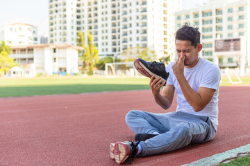 a man disgusted by the smell of his running shoe. A sport man sitting on the  track race at stadium.