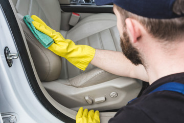 Cleaning service. Man in uniform and yellow gloves washes a car interior in a car wash