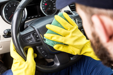 Cleaning service. Man in uniform and yellow gloves washes a car interior in a car wash