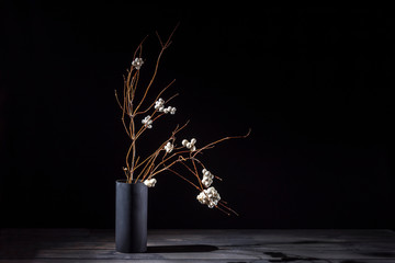 Branch of a bush of a snowberry in a vase on a dark background. Ikebana.