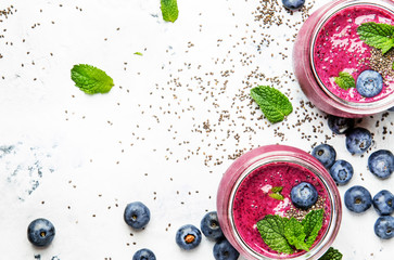 Purple smoothie with blueberries, chia seeds and mint leaves in glass jars on white background,...