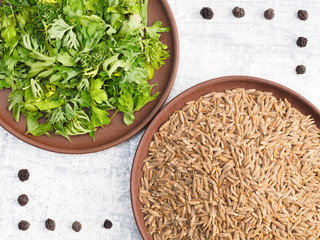 Cumin (jeera) and green herb in a clay plate, black pepper on a white concrete background