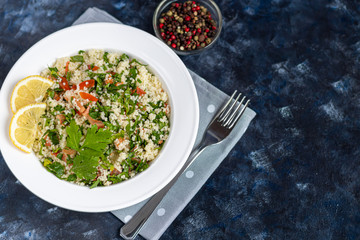 Tabbouleh  salad in a round plate on a wooden background. salad in a white plate on a dark blue, trendy background 2020.