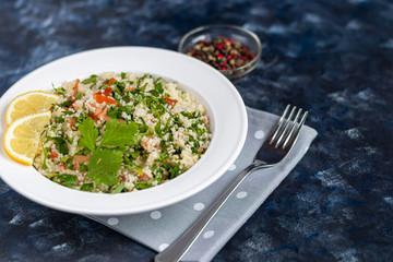 Tabbouleh  salad in a round plate on a wooden background. salad in a white plate on a dark blue, trendy background 2020.