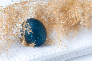 The blue Easter egg is covered with fluffy dry grass on a white napkin. Colored eggs are a symbol...