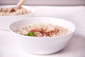 Oatmeal porridge in the white bowl on the white table. Health breakfast. Close up