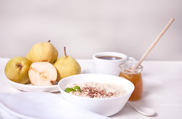 Oatmeal porridge in the white bowl, a bowl of pears, honey and cup of coffee on the background. Health breakfast. Close up.