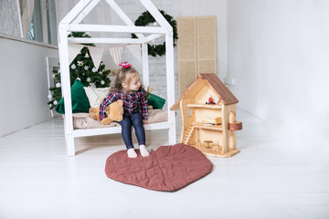 Baby Girl  playing with wooden doll house stuffed with mini furniture toys and doll. A funny little child in a plaid shirt and jeans enjoys in the children's room
