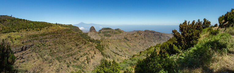 Fototapeta na wymiar Panoramic view of Tenerife Island with volcano Teide above horizon and Los Roques peaks near Garajonay national park at La Gomera. Thickets of relic laurels and heather on steep green slopes. Canary