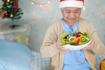 Asian senior or elderly old lady woman patient with Santa Claus helper hat holding salad vegetable healthy food in christmas and new year celebration festival holiday party in hospital.
