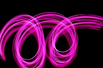 Long exposure photograph of neon pink colour in an abstract swirl, parallel lines pattern against a black background. Light painting photography.