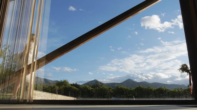 Bride holding the hem of the dress in her hands and the groom in in white shirt and suspenders take turns outside the window against the blue sky.