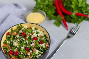 Tabule salad in a round plate on a light gray background under concrete.