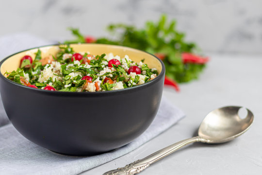 Tabule salad in a round plate on a light gray background under concrete.
