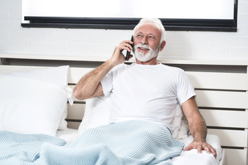 Senior man using mobile phone in bed in his room