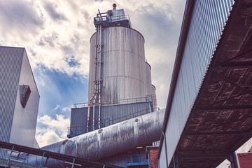 three silos and a large pipe of a factory with dramatic sky