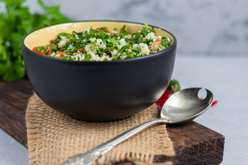 Tabbouleh  salad in a round plate on a light gray background under concrete.