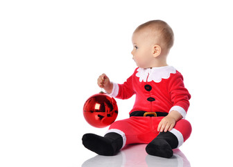 Little child boy toddler in santa claus costume is holding christmas tree red ball fir decoration looking at copy space