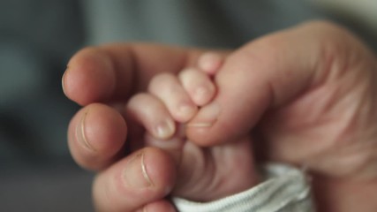 Hand in hand. Grandmother holds the hand of a newborn. Little tinny newborn baby holding finger of the granny. - Powered by Adobe