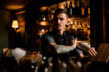 Confident and brutal male bartender posing with shaker