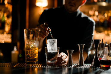 Bartender putting precisely ice cube in cocktail glass