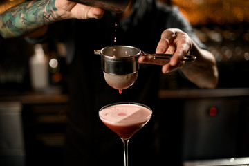 Fototapeta na wymiar Close-up of bartender pouring drink through sieve