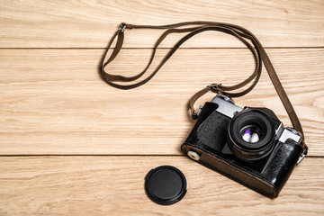 Old retro camera and lens cap on a light wooden background. View from above. Close-up. Free space for text.