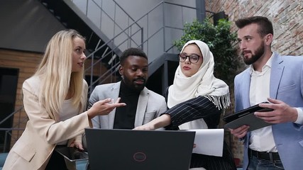 Brainstorm, four multi-ethnic business people uses laptop and computer tablet while discussing financial deal at modern boardroom - Powered by Adobe