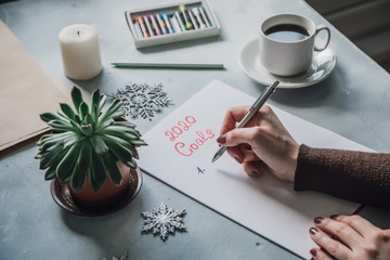 Female hand write2020 Goals list on succulents table, coffee cup top view