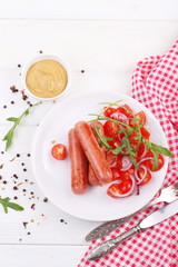 Fried sausages with tomatoes, onions, arugula and mustard on a white wooden background