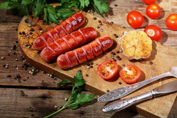 Sausages on a wooden board with tomatoes, garlic and herbs