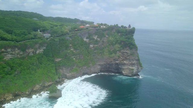 Aerial footage of green cliff and blue ocean with breaking waves in Uluwatu Temple, Exotic tropical nature on Bali, Indonesia.